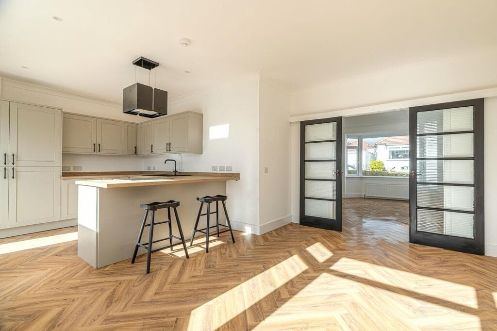 Fitted kitchen with pale cabinets, a timber island top and oak herringbone flooring